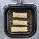 Spanakopita rolls in the bakset of an air fryer, uncooked