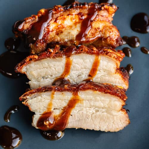 Crispy air fryer pork belly, sliced on a blue plate and drizzled with sauce