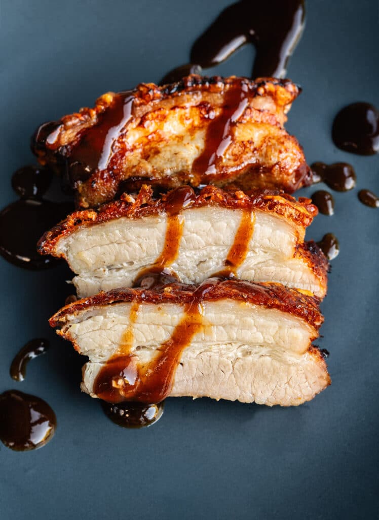 Crispy air fryer pork belly, sliced on a blue plate and drizzled with sauce