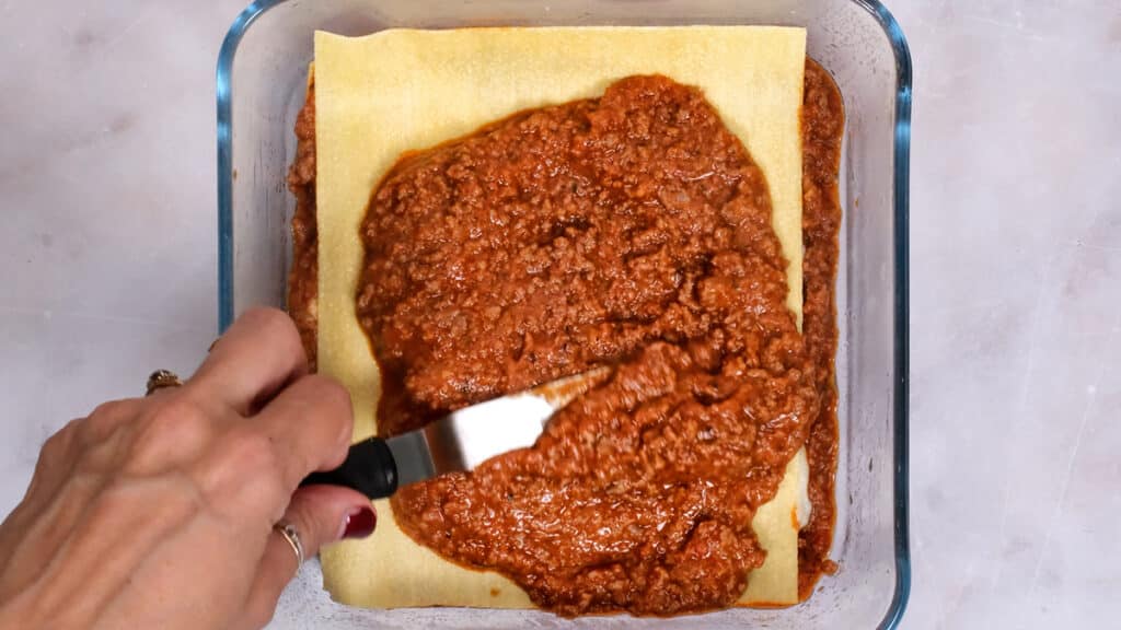 spreading meat sauce over lasagna noodle