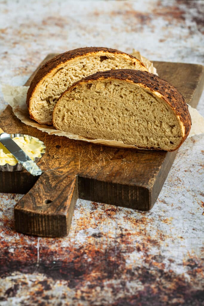 Dutch Crunch Bread sliced in two pieces on a rustic cutting board