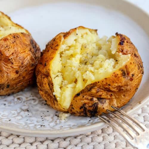Two Air Fryer Baked Potatoes on a plate, one sliced to show the inside