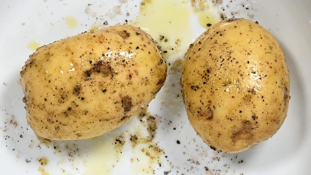 two baking potatoes drizzled with olive oil and seasoned with salt and pepper