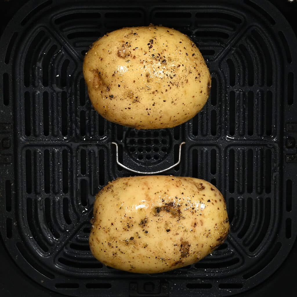 two baking potatoes in the basket on an air fryer