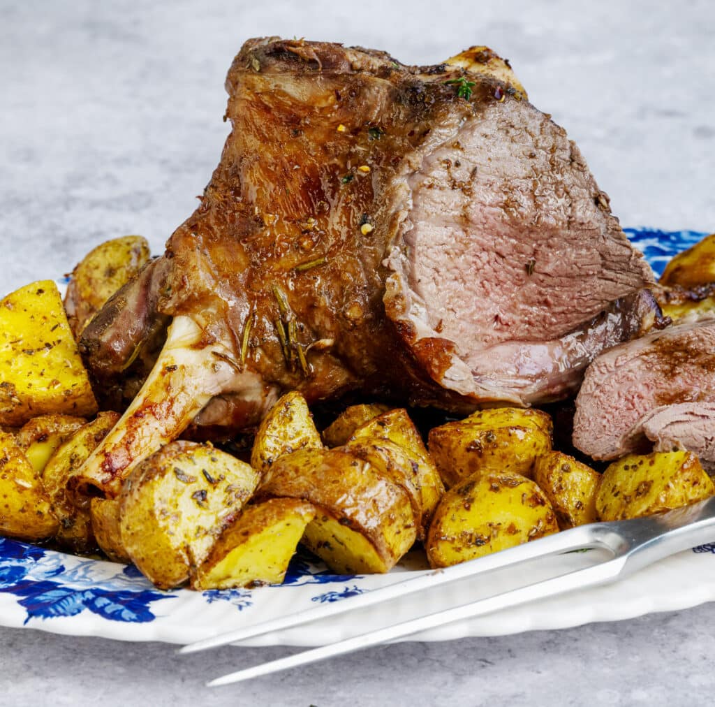 roast half leg of lamb with potatoes on a platter