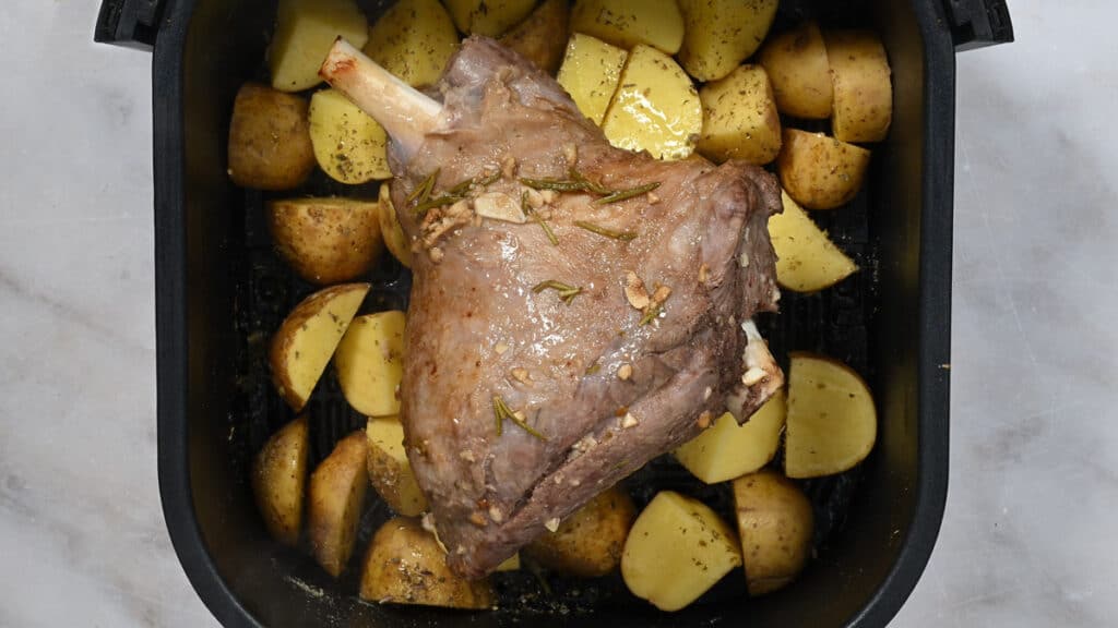 potatoes and half leg of lamb in the basket of an air fryer