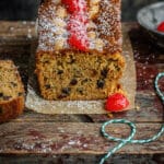 Mary Berry Mincemeat loaf cake decoarated with almonds and cherries, one slice cut, on a wooden board