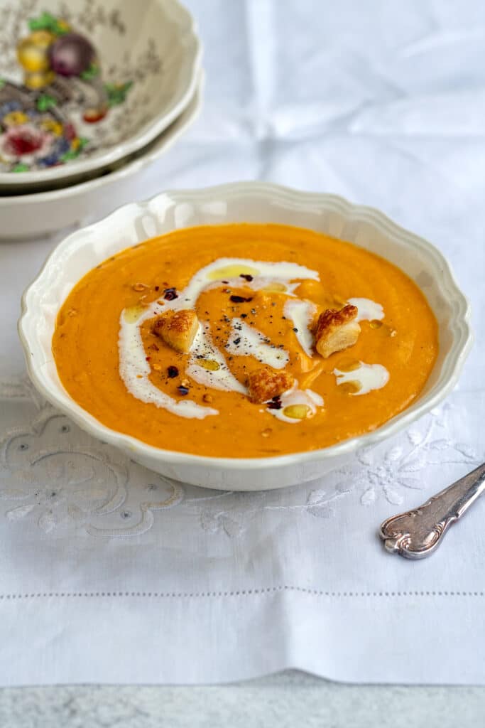 roasted butternut soup in a bowl garnished with cream, olive oil and crushed chili flakes