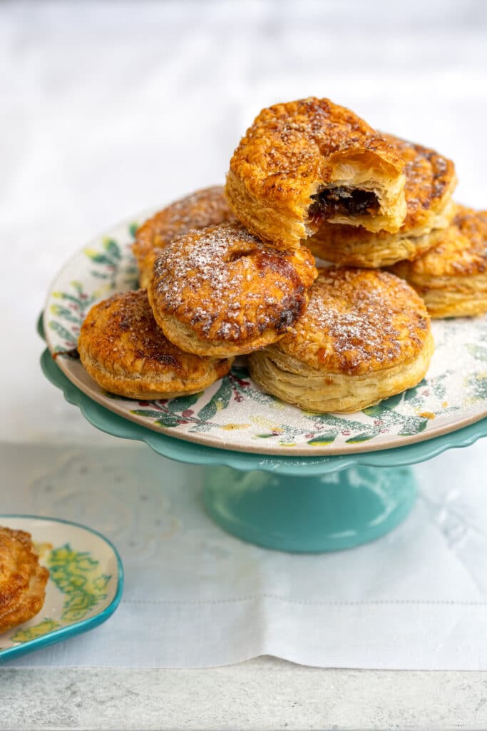 puff pastry mince pies piled on a cake stand, one with a bite taken out