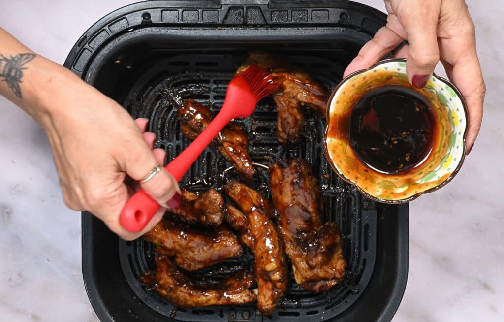 brushing pork ribs with barbecue sauce in an air fryer basket