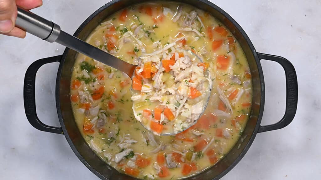 Chicken lemon and rice soup in a pot with a ladle taking a scoop out