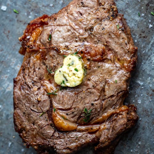 Air fryer rib eye steak on a zinc surface, topped with a pat of garlic butter