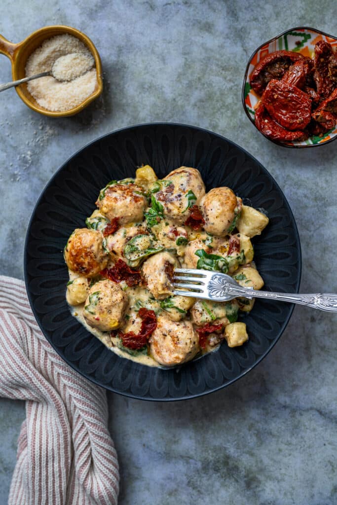 fork spearing a chicken meatball in a bowl serving of meatballs with gnocchi