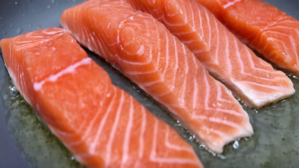close up on salmon fillets cooking in a pan