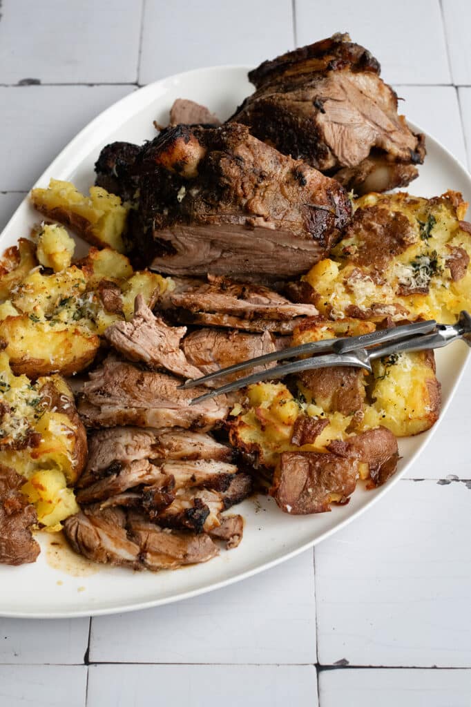 Sliced roast lamb with smashed potatoes on a white platter