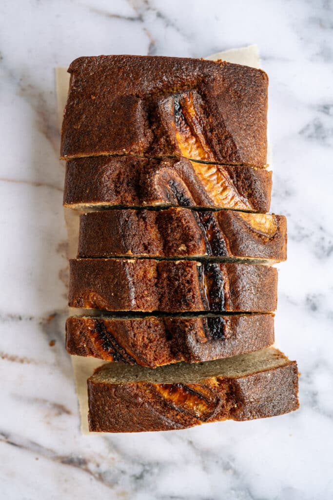 overhead photo of sliced loaf of banana bread on a marble background