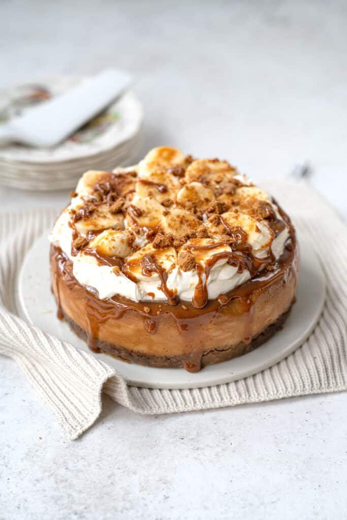 Banoffee Cheesecake topped with whipped cream, bananas and caramel drizzle on a ceramic cake plate