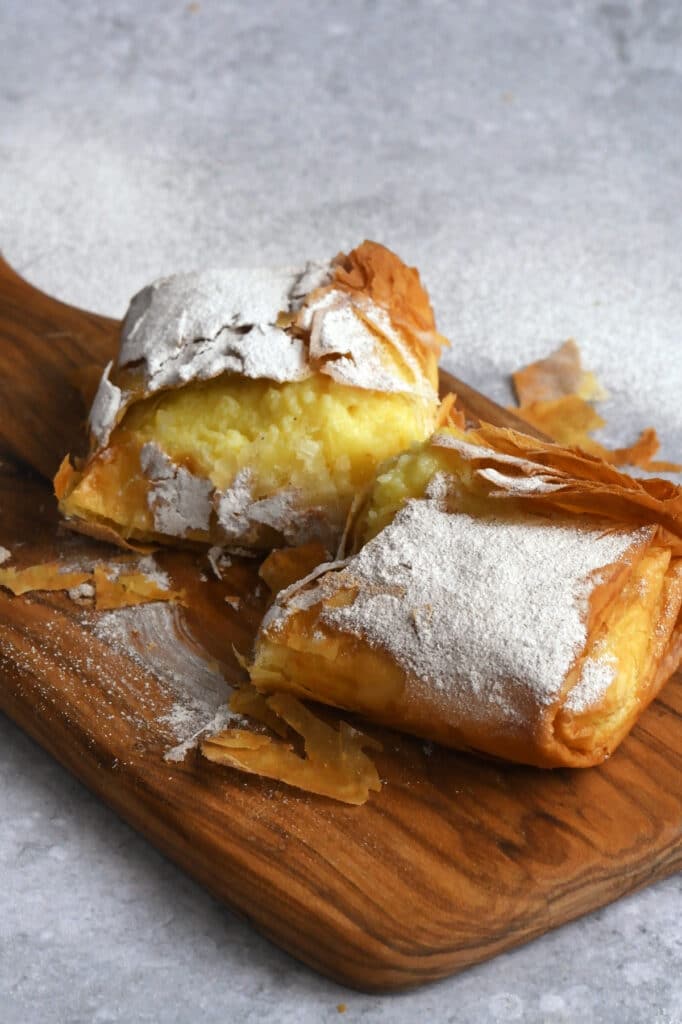 Bougatsa pastry, dusted with powdered sugar and cinnamon on a wooden board, sliced in half
