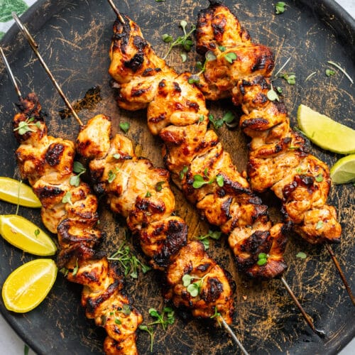 Air Fryer chicken kebabs on a wooden plate with lemon wedges on the side