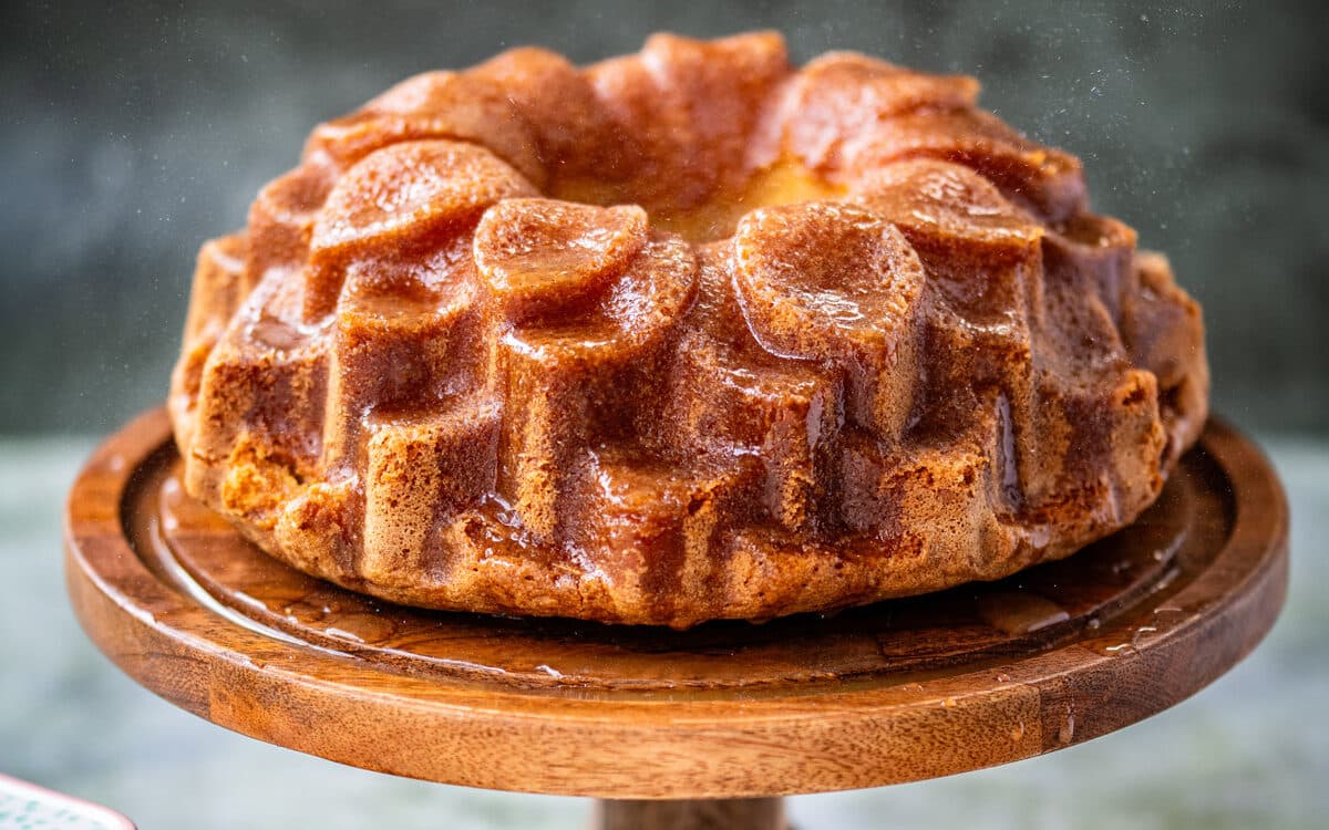 Bacardi rum cake baked in a blossom Bundt pan on a cake stand, rum glaze jug on the side