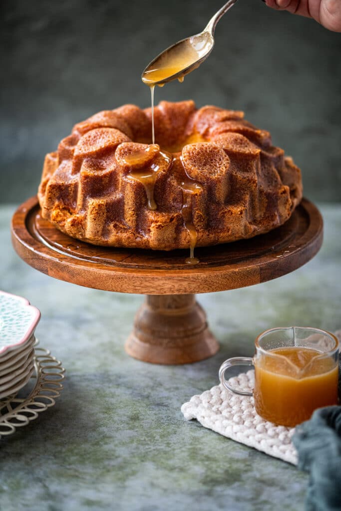 Bacardi rum cake on a cake stand being drizzled with rum glaze
