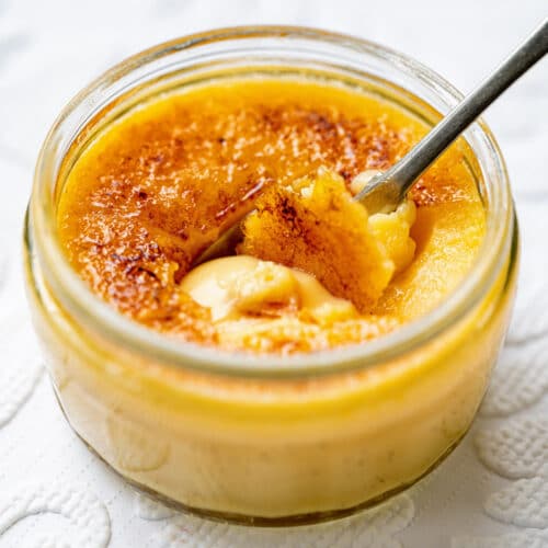 Vanilla creme brulee in a glass ramekin with a spoon having broken the caramelised sugar topping