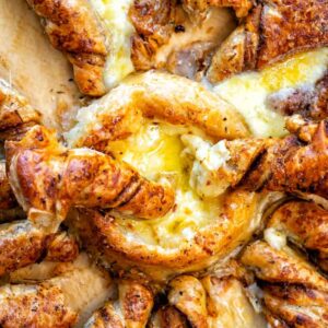 Golden, flaky Pull-Apart Brie Puff Pastry Appetizer twisted into a star shape, filled with gooey melted cheese in the center and along each twist, resting on parchment paper.