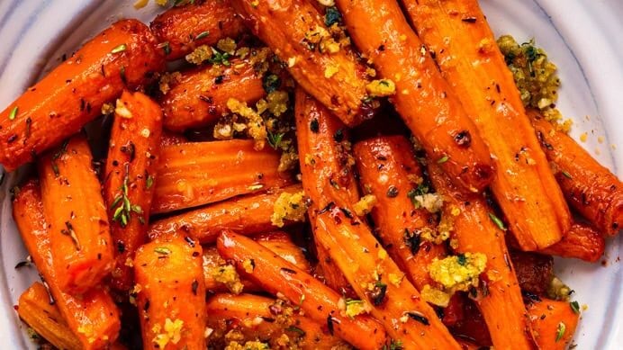 A plate of air fryer roasted carrots garnished with herbs and breadcrumbs, served with a spoon on a white dish against a light blue background.