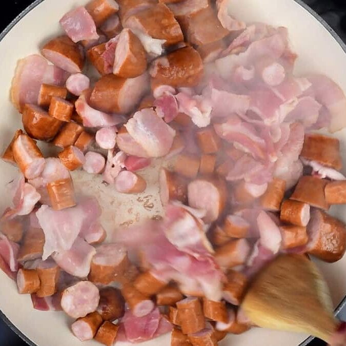 Pan frying bacon and Polish sausages in a large casserole