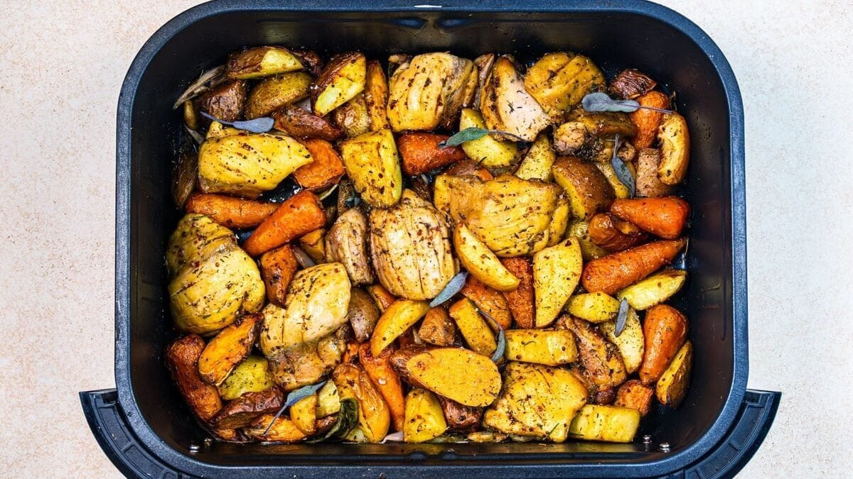 Chopped seasoned potatoes, carrots, and onions roasted in an air fryer basket, garnished with herbs.
