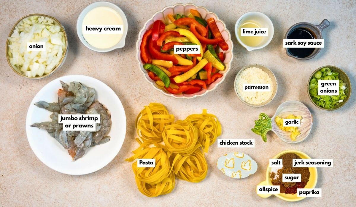 Top-down view of labeled ingredients for a shrimp pasta dish, including chopped onions, heavy cream, sliced peppers, lime juice, soy sauce, green onions, jumbo shrimp, pasta, chicken stock, parmesan, garlic, and seasonings.