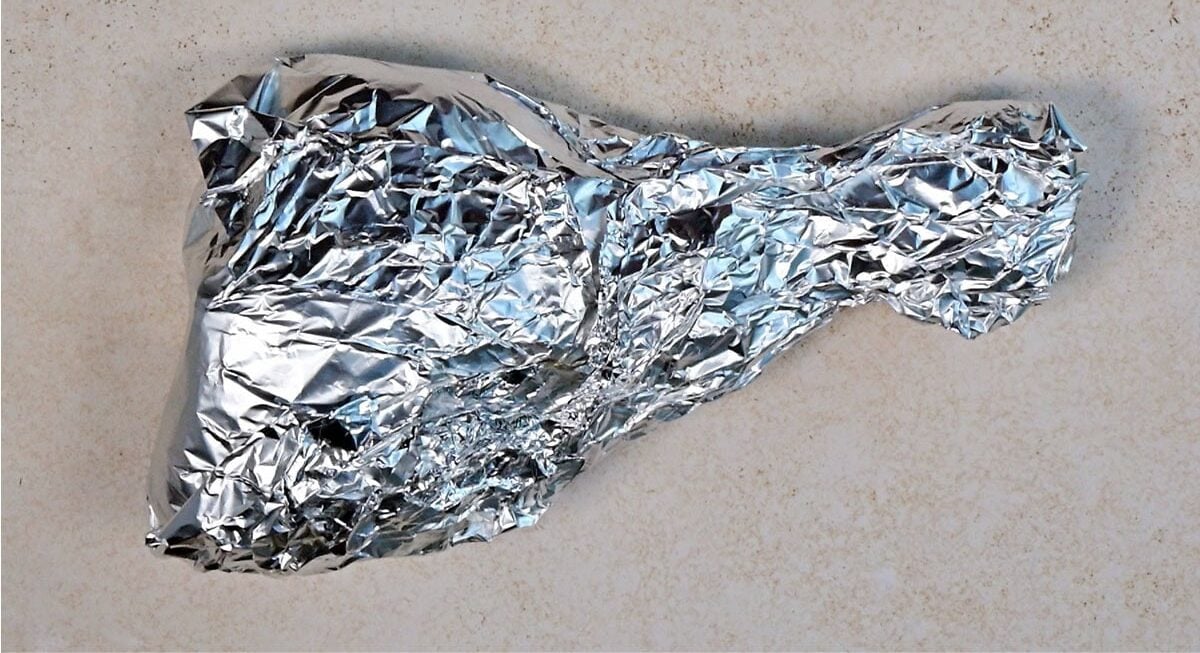 A crumpled sheet of aluminum foil is shaped like a drumstick and placed on a light, textured surface.