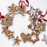 A wreath made of decorated gingerbread salt dough ornaments shaped like stars, hearts, and snowflakes, all tied together with red ribbons, arranged on a white background.