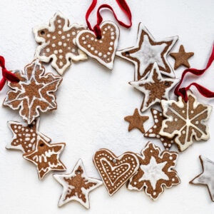 A wreath made of decorated gingerbread salt dough ornaments shaped like stars, hearts, and snowflakes, all tied together with red ribbons, arranged on a white background.