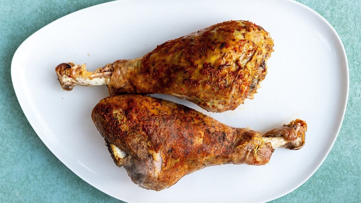 Two seasoned and roasted turkey legs placed side by side on a white oval plate, set against a light green background.