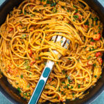 A pan filled with creamy crawfish pasta cooked in one saucepan, mixed with small pieces of seafood and garnished with chopped herbs. A slotted spoon is resting in the pasta, ready to serve.