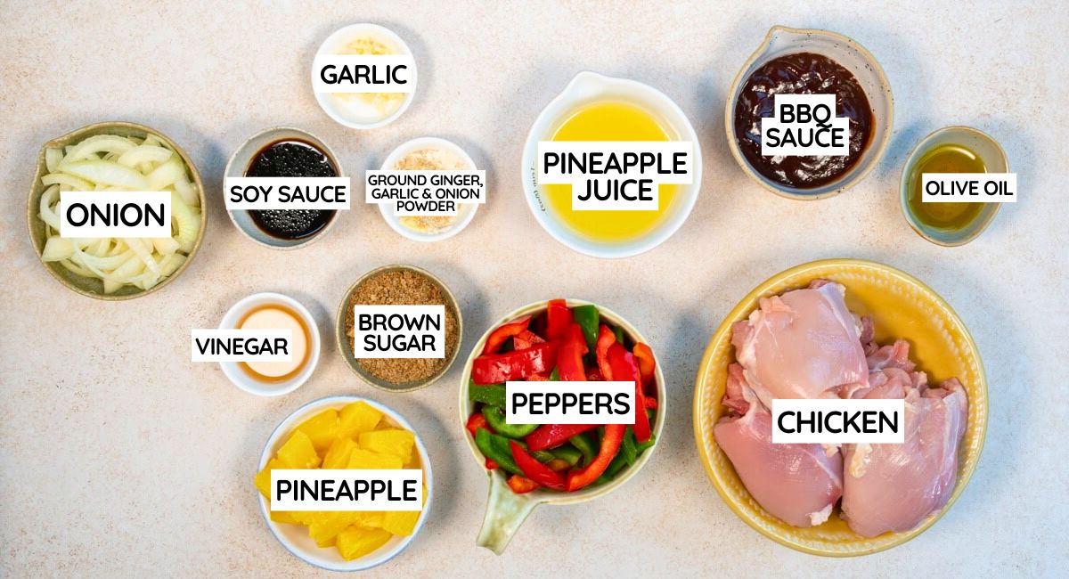 A top-down view of various labeled ingredients in bowls for a chicken dish, including chicken, peppers, pineapple, onion, soy sauce, vinegar, garlic, brown sugar, pineapple juice, BBQ sauce, olive oil, and spices.