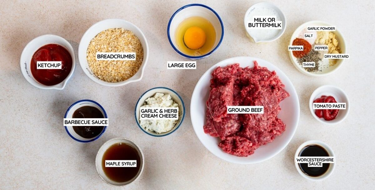 Top-down view of bowls holding ingredients for air fryer meatloaf, including ground beef, breadcrumbs, large egg, garlic & herb cream cheese, ketchup, barbecue sauce, maple syrup, milk, spices, tomato paste, and Worcestershire sauce.