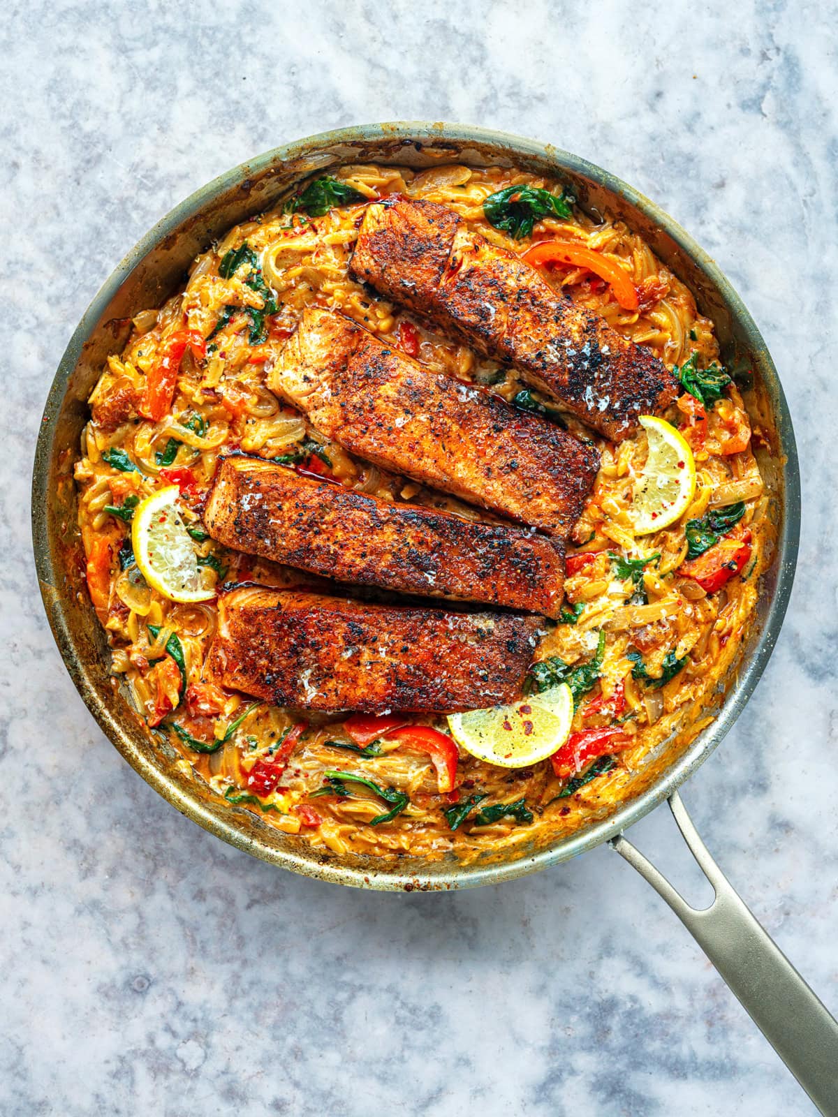 A skillet filled with creamy Cajun Salmon Orzo with sun-dried tomatoes, red peppers, spinach and tomatoes.