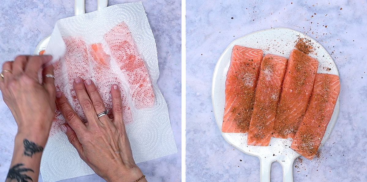 A person pats raw salmon fillets dry with a paper towel on a white plate; next to it, the fillets are seasoned with spices on the same plate, set on a light marble surface.