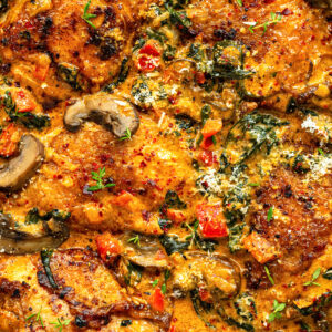 Golden-brown chicken thighs cooked in a creamy chicken paprika sauce with mushrooms, spinach, red bell peppers, and herbs, topped with grated cheese and fresh thyme. This rich, colorful dish bursts with flavor in every bite.