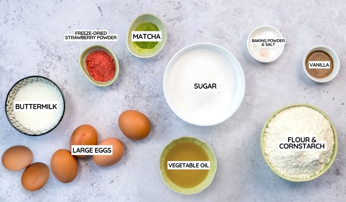 Top-down view of Matcha Cake ingredients labeled on a light surface for a Matcha Chiffon Cake Recipe: buttermilk, large eggs, freeze-dried strawberry powder, matcha, sugar, vegetable oil, flour & cornstarch, baking powder & salt, and vanilla.