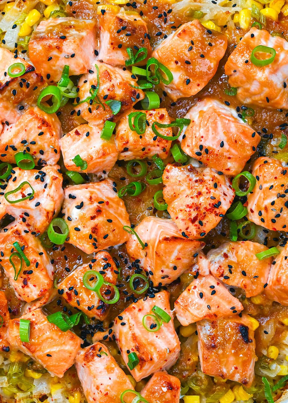 Cubes of cooked salmon topped with chopped green onions and black sesame seeds, arranged on a bed of rice and vegetables.