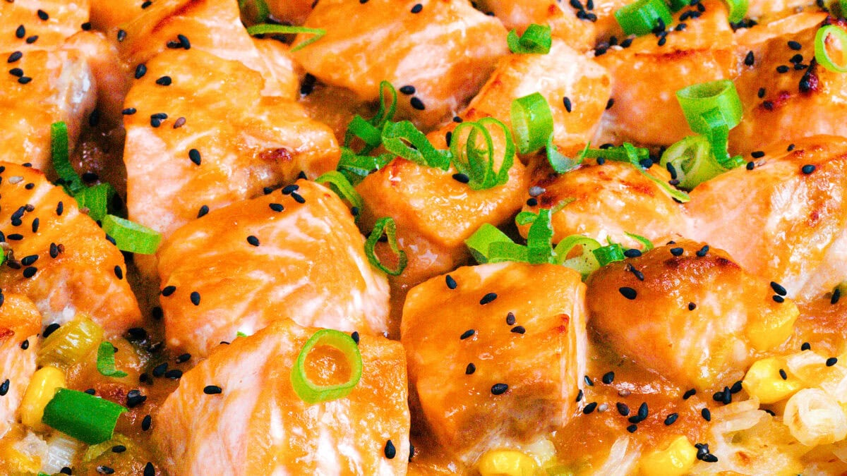 Close-up of cooked salmon chunks topped with chopped green onions and black sesame seeds, mixed with corn and other vegetables, creating a colorful and appetizing dish.