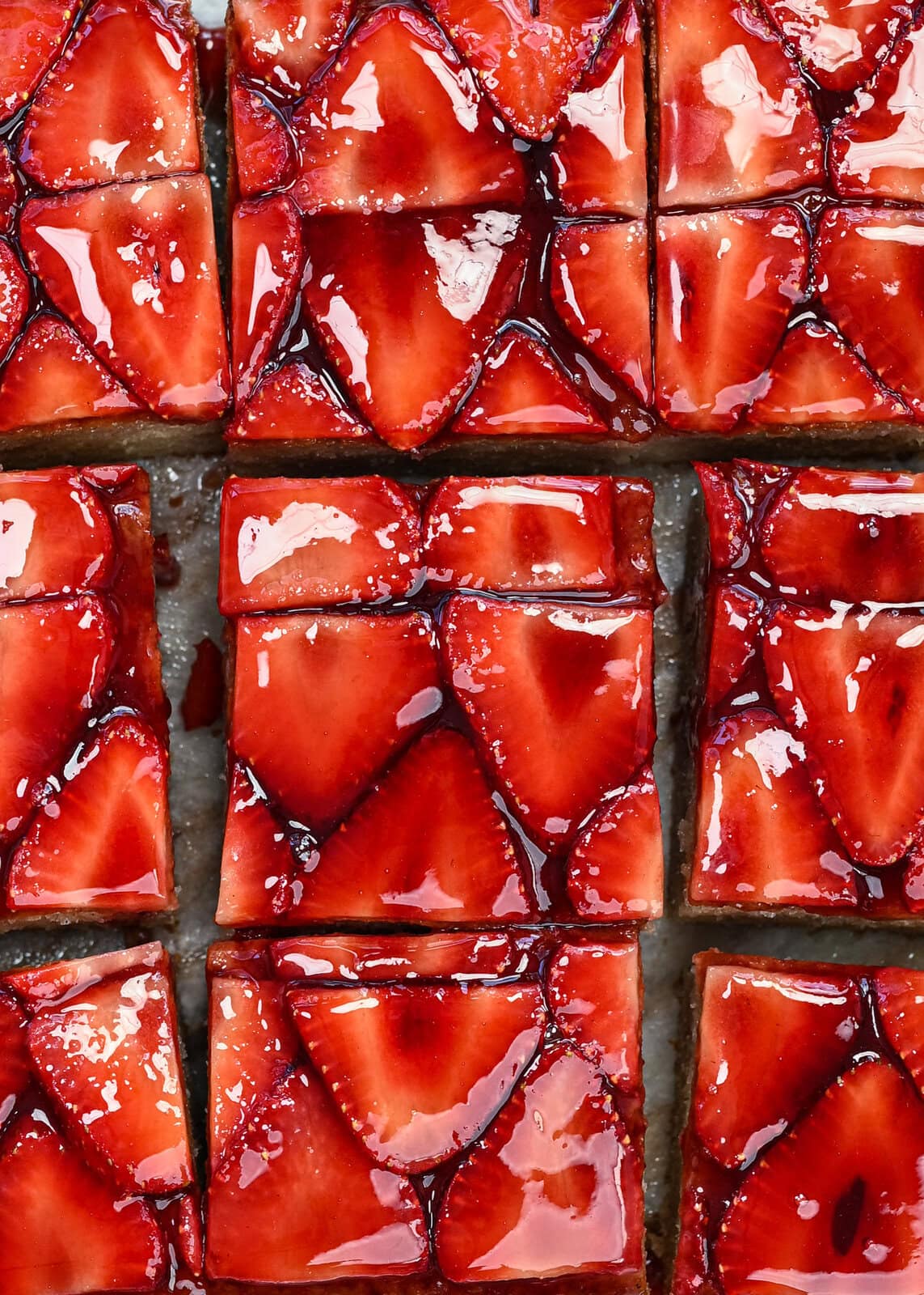 Close-up of glossy strawberry tart slices, arranged in a grid pattern. The strawberries are thinly sliced and coated with a shiny glaze, covering a pastry base.