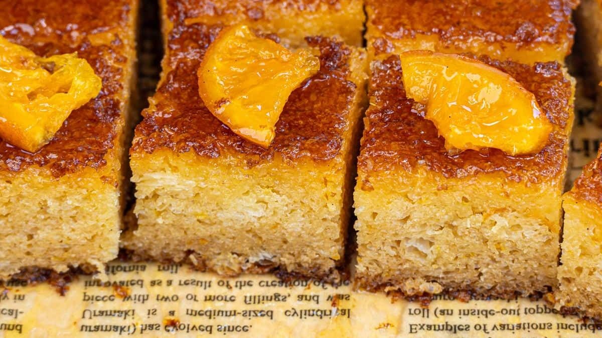 Rectangular slices of moist orange cake are topped with glossy orange segments and arranged neatly on a parchment sheet with printed text.