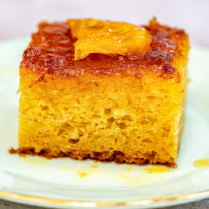 A close-up of a slice of moist portokalopita orange phyllo cake with caramelized orange pieces on top, served on a white plate with a gold rim.