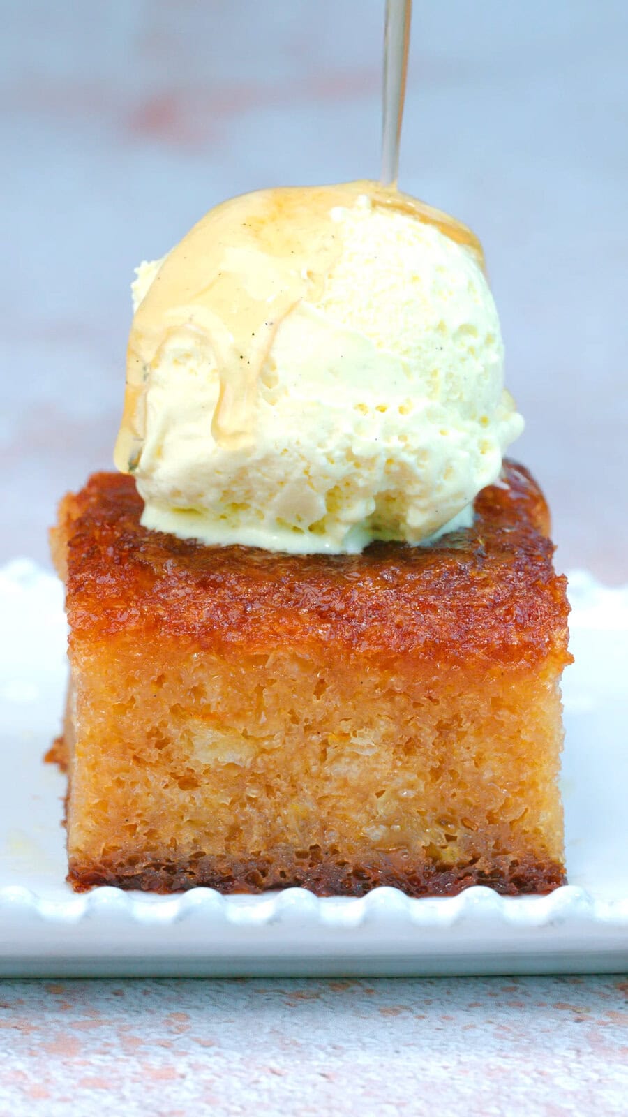 A thick slice of golden, moist cake topped with a scoop of vanilla ice cream and drizzled with honey, served on a white plate.