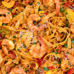 Close-up of creamy fettuccine pasta with shrimp, bell peppers, zucchini, Parmesan cheese, and herbs mixed together in a colorful, appetizing dish.