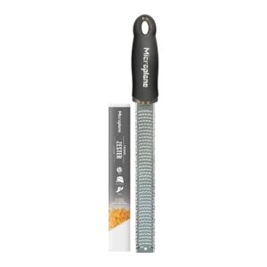 A Microplane zester with a black handle is shown next to its packaging, which features an image of zested orange peel and product details.